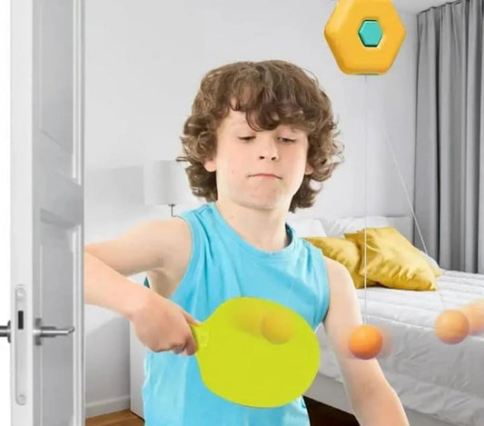 Young boy practicing his hand-eye coordination inside a bedroom using a yellow hexagon-shaped door-hanging table tennis trainer tool.